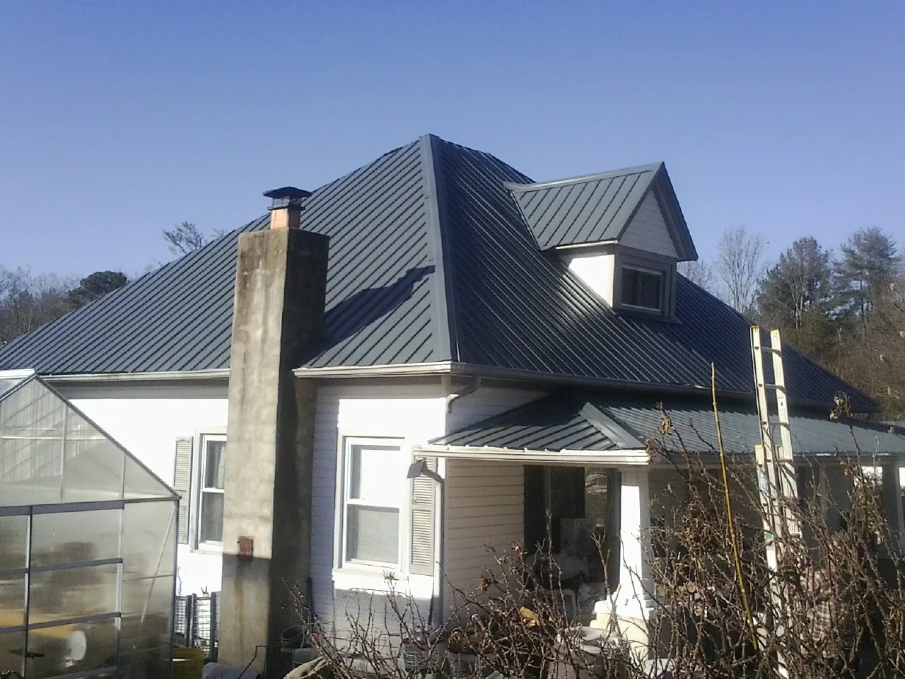 Dark blue standing seam metal roof on a white farmhouse with dormer — Slate & Tile Roof Repair by Roofing Brothers in Mascotte