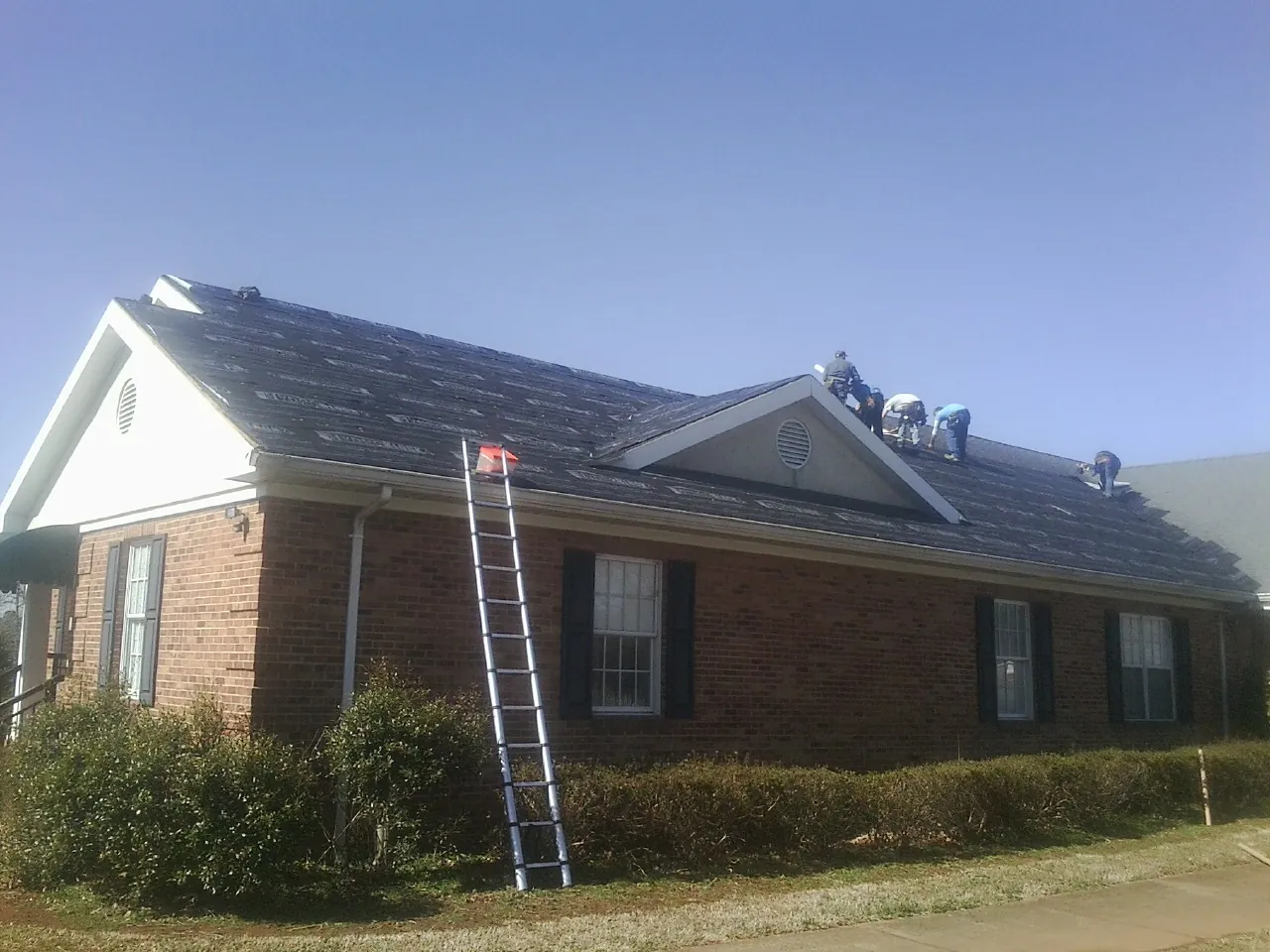 Crew tearing shingles off a brick ranch roof with a ladder set — Metal Roof Repair work by our crew in Mascotte