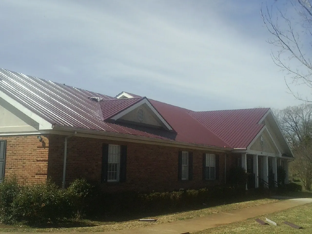 Red metal roof with gabled entries on a long brick building, from a Hail Damage Roof Repair job in Mascotte