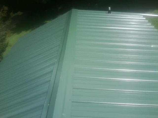 New green metal panels meeting at the ridge of a roof — Flat Roof Repair work by our crew in Mascotte