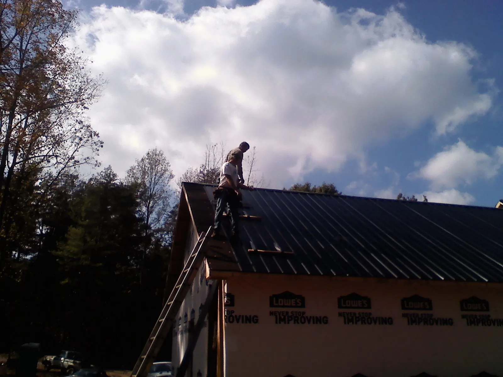 Roofer fastening dark metal panels high against a cloudy sky, from a Roof Inspection job in Mascotte