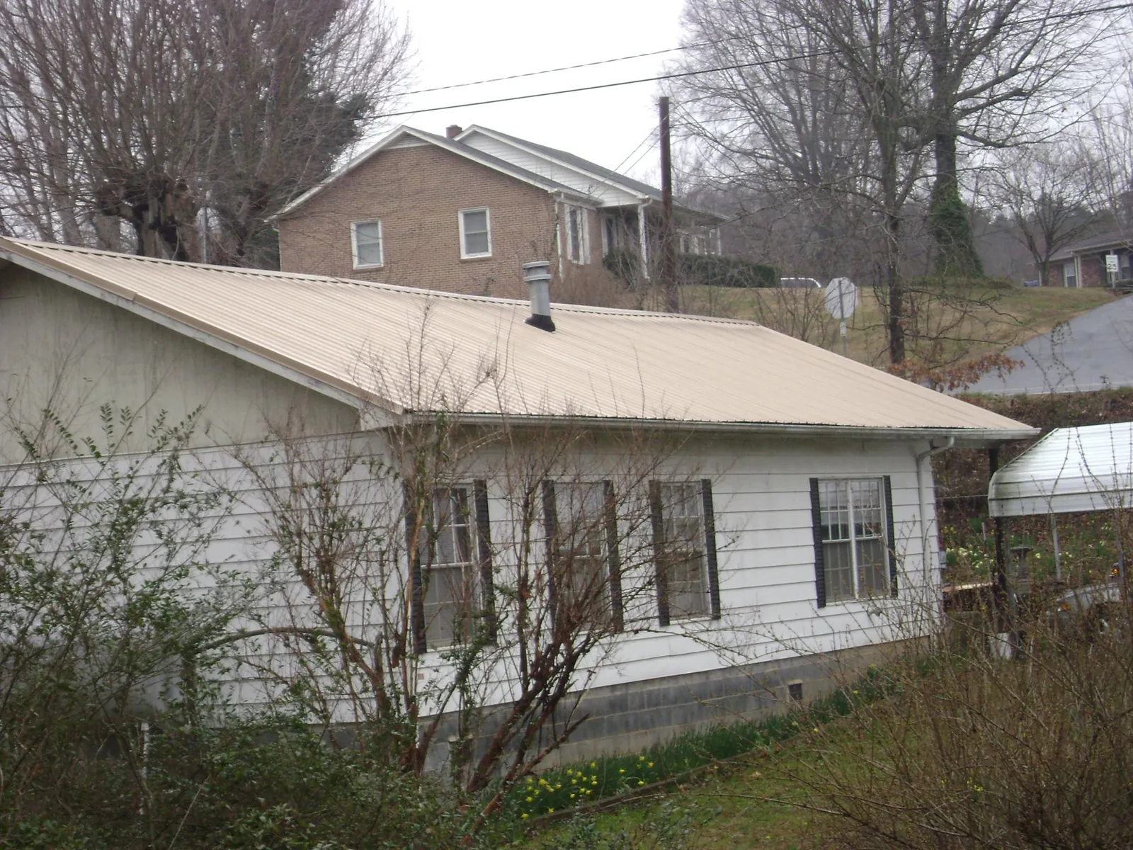 Tan metal roof on a white sided house set into a hillside — Commercial Roofing by Roofing Brothers in Mascotte